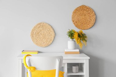 Vazoda mimoza çiçekleri ve ışık duvarı yakınında kitapları olan modern bir işyeri.