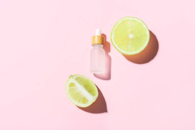 Şişe yağlı ve pembe arka planda olgun bergamot meyvesi parçaları.