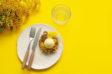 Sarı arka planda mimoza çiçekleri olan Paskalya kutlaması için şık bir masa.