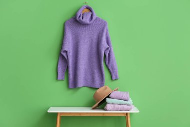 Katlanmış süveter yığını ve yeşil duvarın yanındaki masada keçeli şapka