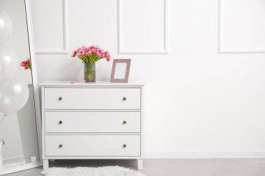Laleli vazo ve boş fotoğraf çerçeveli çekmeceler beyaz duvarın yanındaki odada.