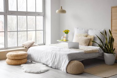 Dizüstü bilgisayarlı rahat bir yatak, laleli vazo ve yatak odasındaki masada Paskalya dekoru.