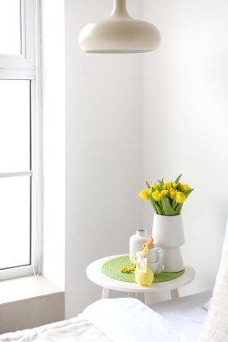 Laleli vazolar, fincanlar ve yatak odasındaki ışık duvarının yanındaki masada Paskalya tavşanları.