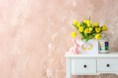 Güzel laleler, tebrik kartı, tavşan ve fener. Renk duvarının yanındaki masada Paskalya dekoru var.