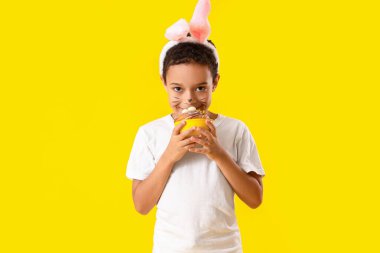 Sarı arka planda Paskalya pastası olan küçük Afro-Amerikalı çocuk.