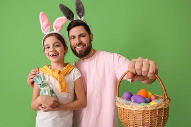 Paskalya pastalı küçük kız, babası ve yumurtaları yeşil arka planda sepette.