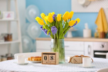 8 Mart tarihli küp takvimi, yemek masasında çiçekler ve hediye kutusu. Uluslararası Kadınlar Günü kutlamaları