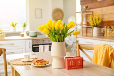 8 Mart tarihli küp takvimi, laleler, tatlı ve kupa yemek masasında. Uluslararası Kadınlar Günü kutlamaları