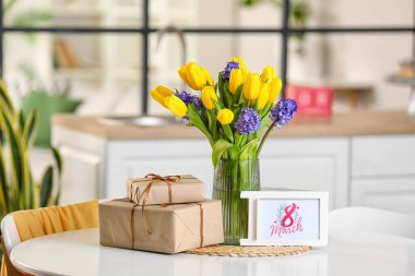 8 Marş yazılı tebrik kartı, yemek masasında çiçekler ve hediye kutuları. Uluslararası Kadınlar Günü kutlamaları