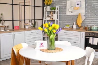 Çiçekli vazo ve yemek masasında 8 Marş yazılı tebrik kartı. Uluslararası Kadınlar Günü kutlamaları