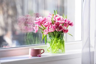 Buket lale çiçekli vazo ve pencere kenarında bir fincan çay.