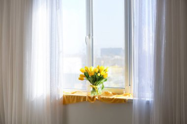 Odadaki pencere eşiğinde sarı lale çiçekleri vazosu