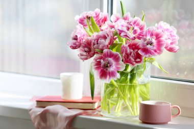 Güzel lale çiçekli vazo, bir fincan çay, pencere kenarında kitap ve mum.