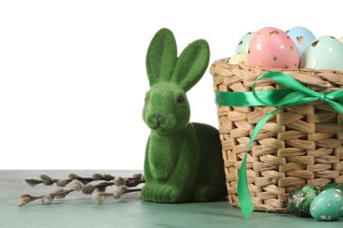 Boyanmış Paskalya yumurtaları, söğüt dalları ve beyaz arka planda duran tavşanlı sepet.