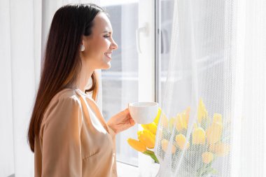 Güzel genç bayan pencerenin yanında sıcak kahve içiyor.