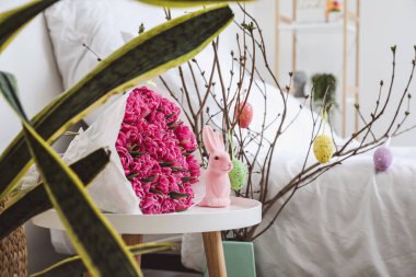 Çiçek buketi, komodindeki Paskalya tavşanı ve yatak odasındaki boyalı yumurtalarla süslenmiş ağaç dalları.