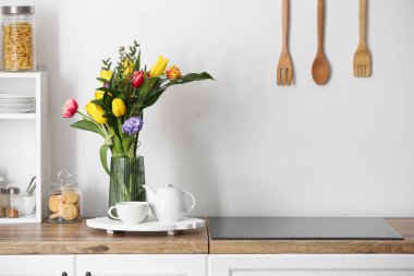 Çiçekli vazo, çaydanlık ve çay bardağı beyaz duvarın yanındaki mutfak tezgahında.