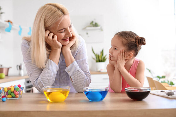 Little girl and her grandmother painting Easter eggs at home