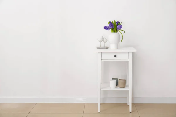 Vase with flowers and stylish decor on standing desk near white wall in room