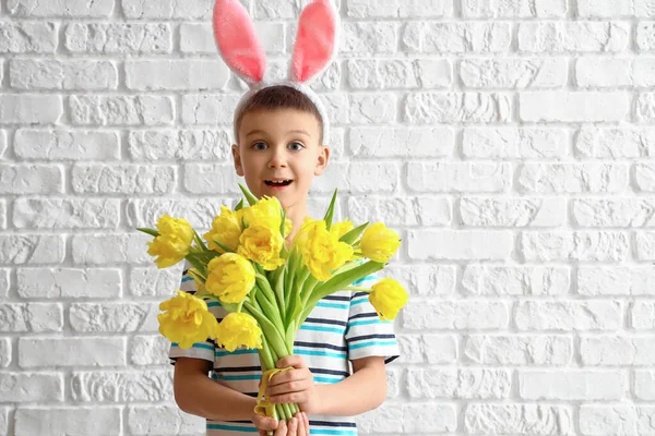 白いレンガの背景にウサギの耳と花を持つかわいい男の子 イースターのお祝い — ストック写真