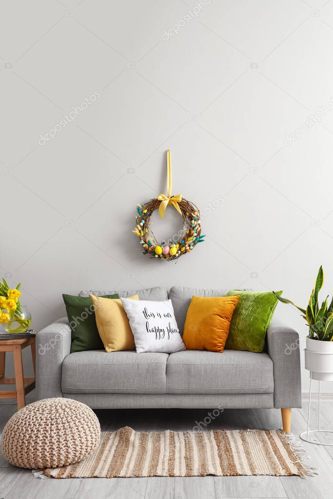 Comfortable sofa near light wall with Easter wreath in living room