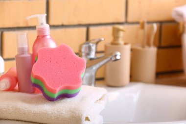 Temiz havlu, banyo süngeri ve lavabonun yanındaki kozmetik ürünleri.