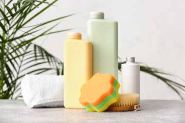 Şişeler dolusu kozmetik ürünler, banyo süngeri, masaj fırçası ve arka planda havlu.