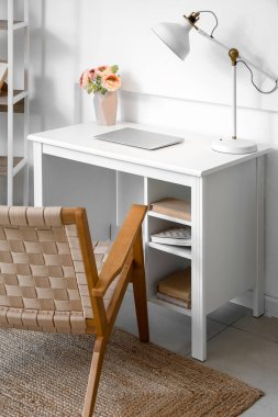 Vazoda çiçekleri, dizüstü bilgisayarı ve lambası olan modern işyeri ofis duvarının yanında.