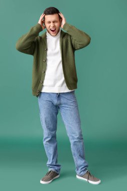 Yeşil arka planda atlayan genç adam bağırıyor.