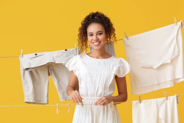 Genç Afro-Amerikalı kadın sarı arka planda ahşap mandal asıyor.