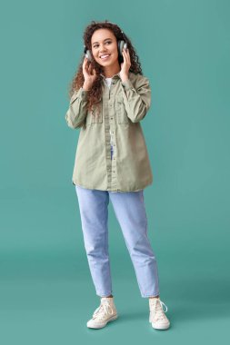 Kulaklıklı genç Afro-Amerikalı kadın yeşil arka planda müzik dinliyor.