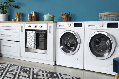 Modern çamaşır makineleri, fırın ve beyaz tezgahı olan şık bir mutfak.