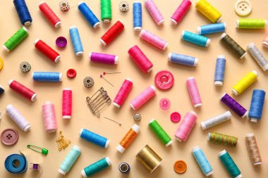 Bej arkaplanda düğmeleri ve iğneleri olan iplik makaraları