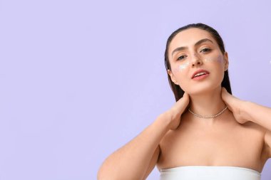 Yaratıcı makyajlı genç bir kadın boyna dokunuyor.