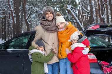 Mutlu aile, karlı kış gününde ormanda arabanın yanında sarılıyor.