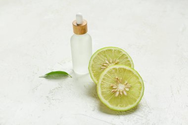 Temel yağlı bir şişe ve arka planda bergamot meyvesi dilimleri.