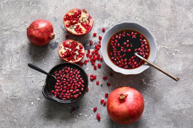 Bir kase nar pekmezi ve gri arka planda taze meyveler.