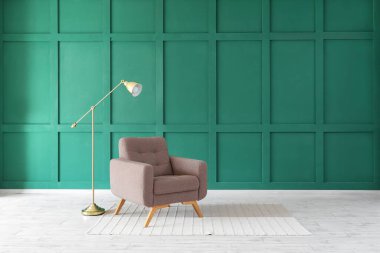 Yeşil duvarın yanında koltuk ve halı olan standart lamba.
