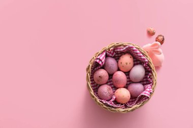 Paskalya yumurtası boyanmış sepet ve pembe arka planda tavşan.
