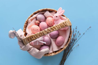 Mavi arka planda boyanmış Paskalya yumurtaları, lavanta ve tavşan sepeti.