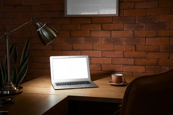 Modern Workplace Laptop Cup Coffee Glowing Lamp Brick Wall Dark — Stock Photo, Image