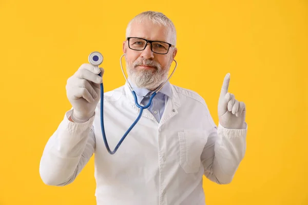 Ώριμος Άνδρας Γιατρός Στηθοσκόπιο Που Δείχνει Κάτι Κίτρινο Φόντο — Φωτογραφία Αρχείου