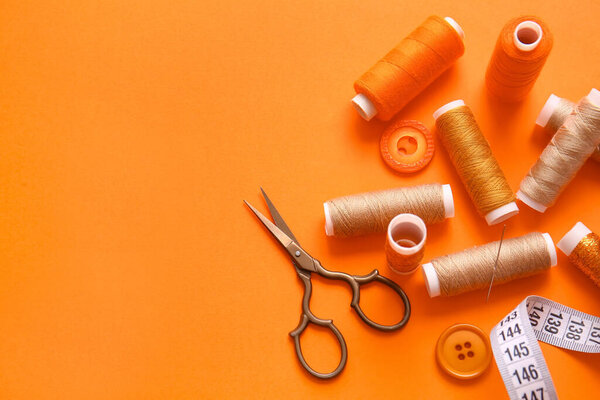 Thread spools with measuring tape, scissors and buttons on orange background