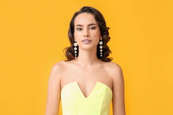 Pretty young woman with glitters on her face against yellow background