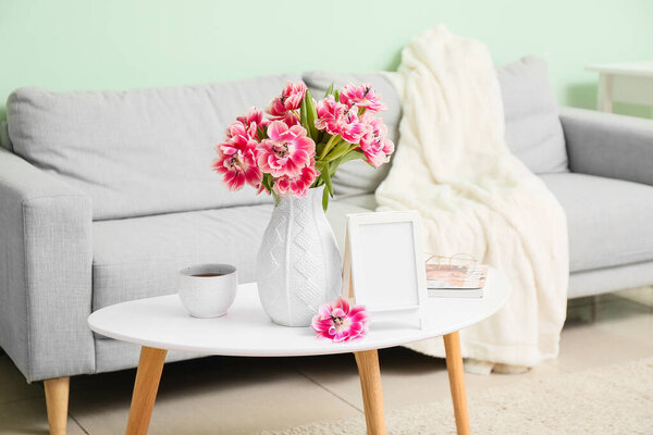 Vase with beautiful tulips, photo frame and cup of tea on table in room. International Woman's Day celebration