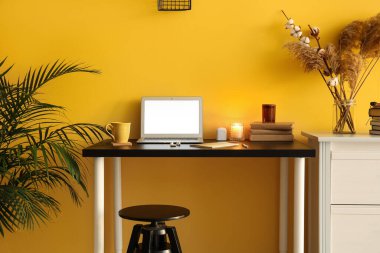 Modern dizüstü bilgisayar, kulaklık, bardak ve yanan mumlar renkli duvarın yanındaki masada.