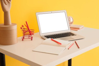 Kırtasiye malzemeleri ve modern laptop renkli duvarın yanındaki masada.