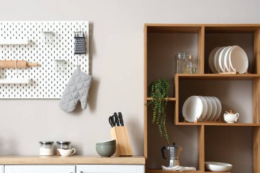 Mutfak duvarının yanında bulaşık takımı, kahve makinesi ve ev bitkisi olan ahşap raf ünitesi.