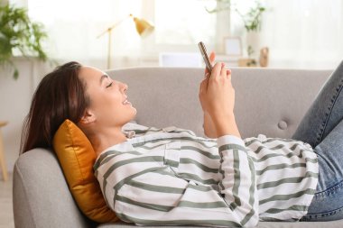 Kanepeye uzanmış cep telefonuyla e-posta gönderen genç bir kadın.