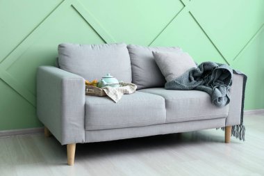 Yeşil duvarın yanındaki şık kanepede çaydanlıklı tepsi.